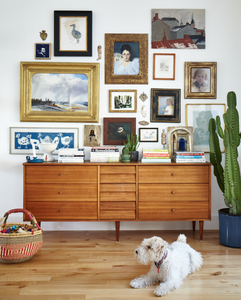 Gallery wall above a brown dresser with a cute white dog in front.